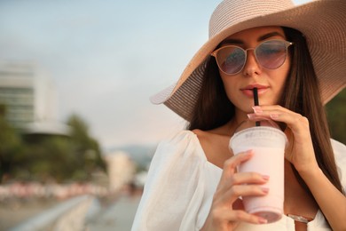 Photo of Beautiful young woman with tasty milk shake outdoors, space for text