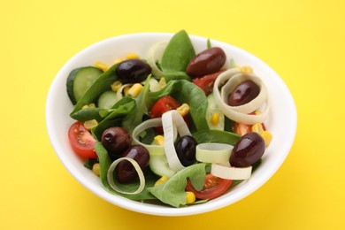 Photo of Bowl of tasty salad with leek and olives on yellow table, closeup