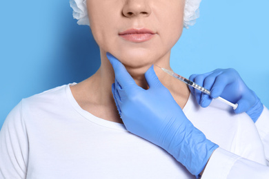 Photo of Mature woman with double chin receiving injection on blue background, closeup