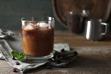 Photo of Glass of delicious iced coffee with milk, mint and beans on wooden table, space for text