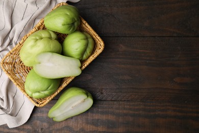 Photo of Cut and whole chayote in wicker basket on wooden table, flat lay. Space for text