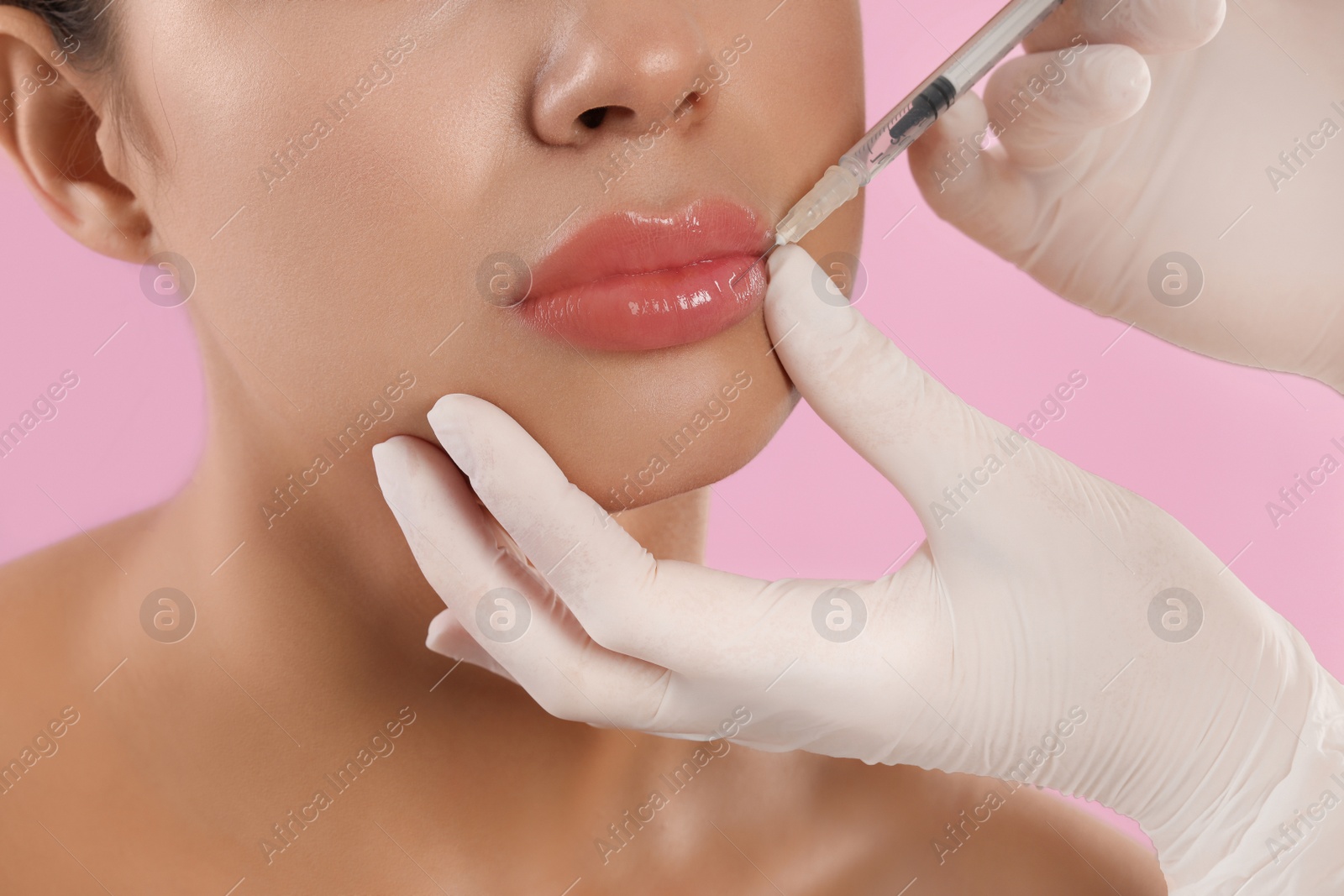 Photo of Young woman getting lips injection on pink background, closeup