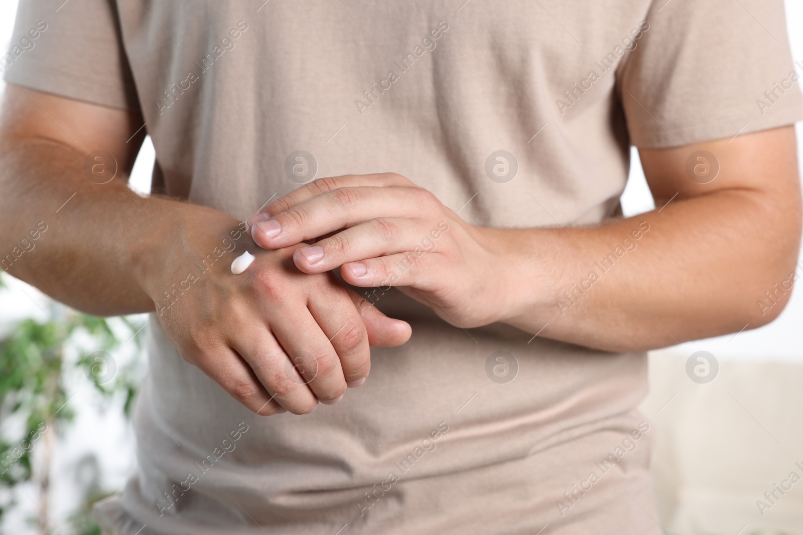 Photo of Man applying hand cream at home, closeup