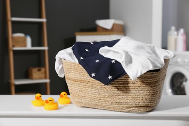 Laundry basket with baby clothes and rubber ducks on table in bathroom