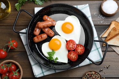 Photo of Romantic breakfast with fried sausages and heart shaped eggs on wooden table, flat lay. Valentine's day celebration