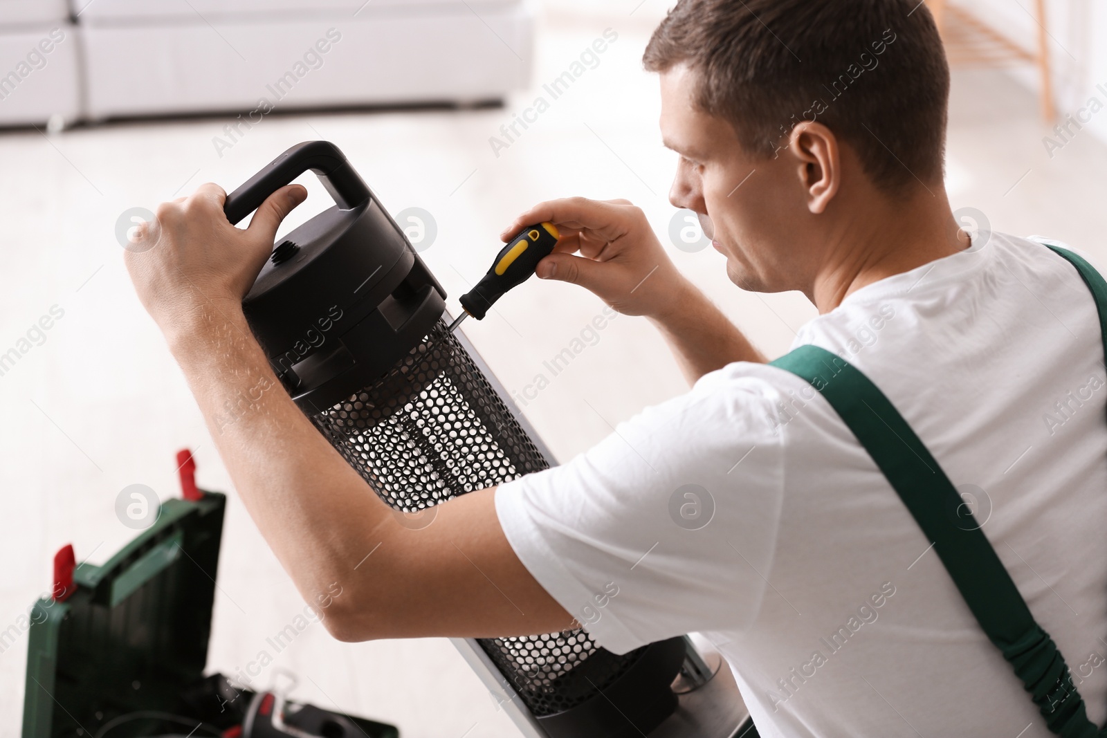 Photo of Professional technician repairing electric patio heater with screwdriver indoors