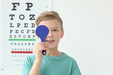 Cute little boy near eye chart in ophthalmologist office