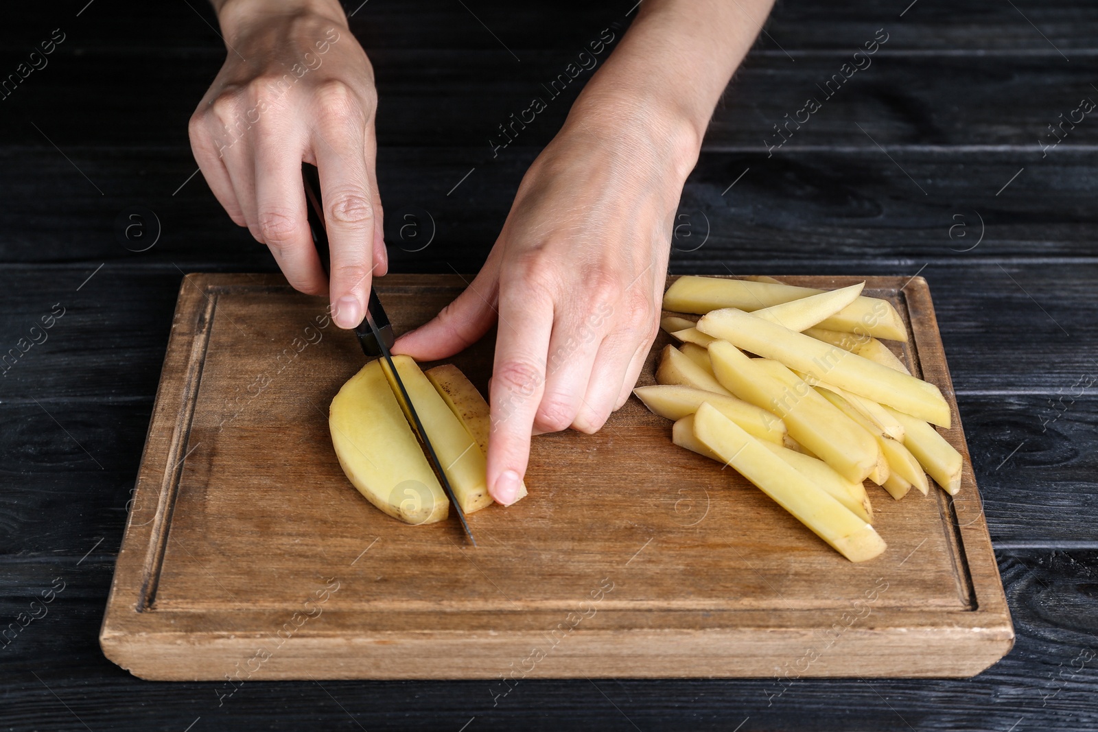 Photo of Woman cut potatoes on black wooden table, closeup