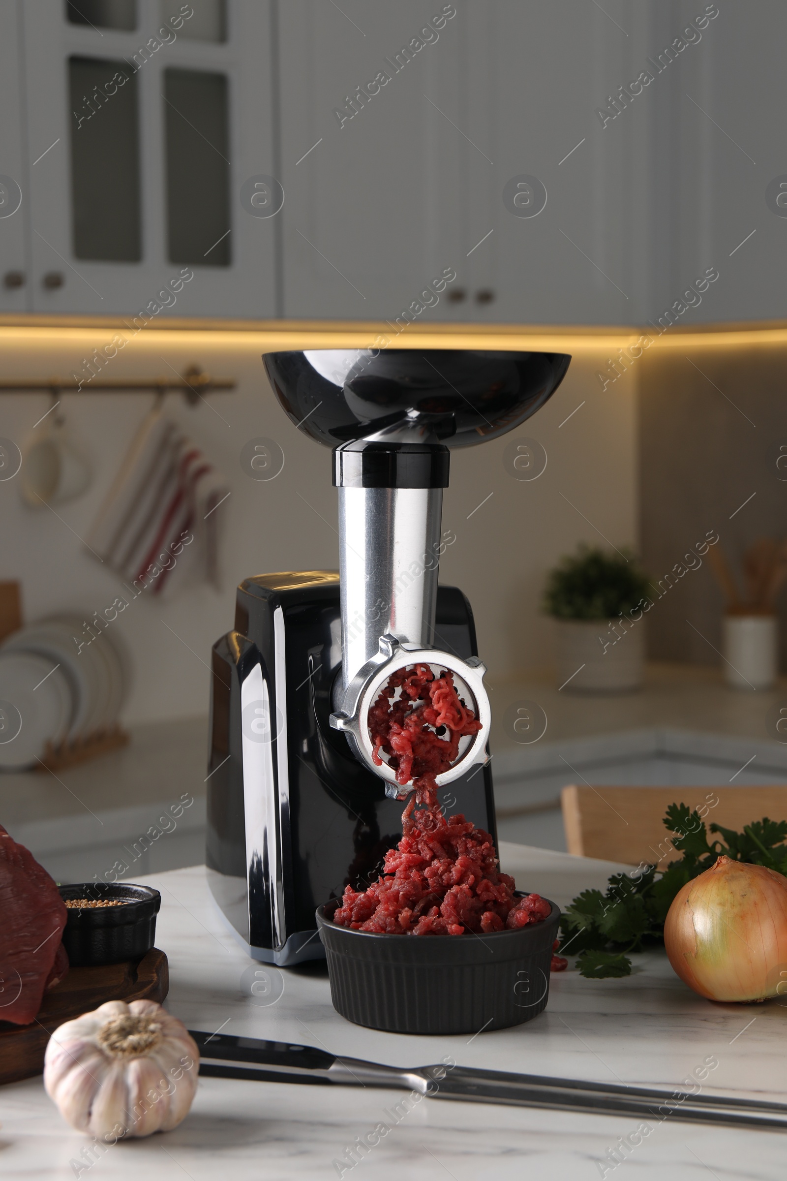 Photo of Electric meat grinder with beef mince and products on white marble table in kitchen