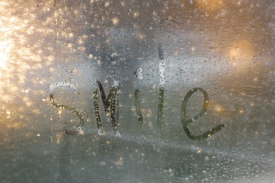 Photo of Word Smile written on foggy window. Rainy weather