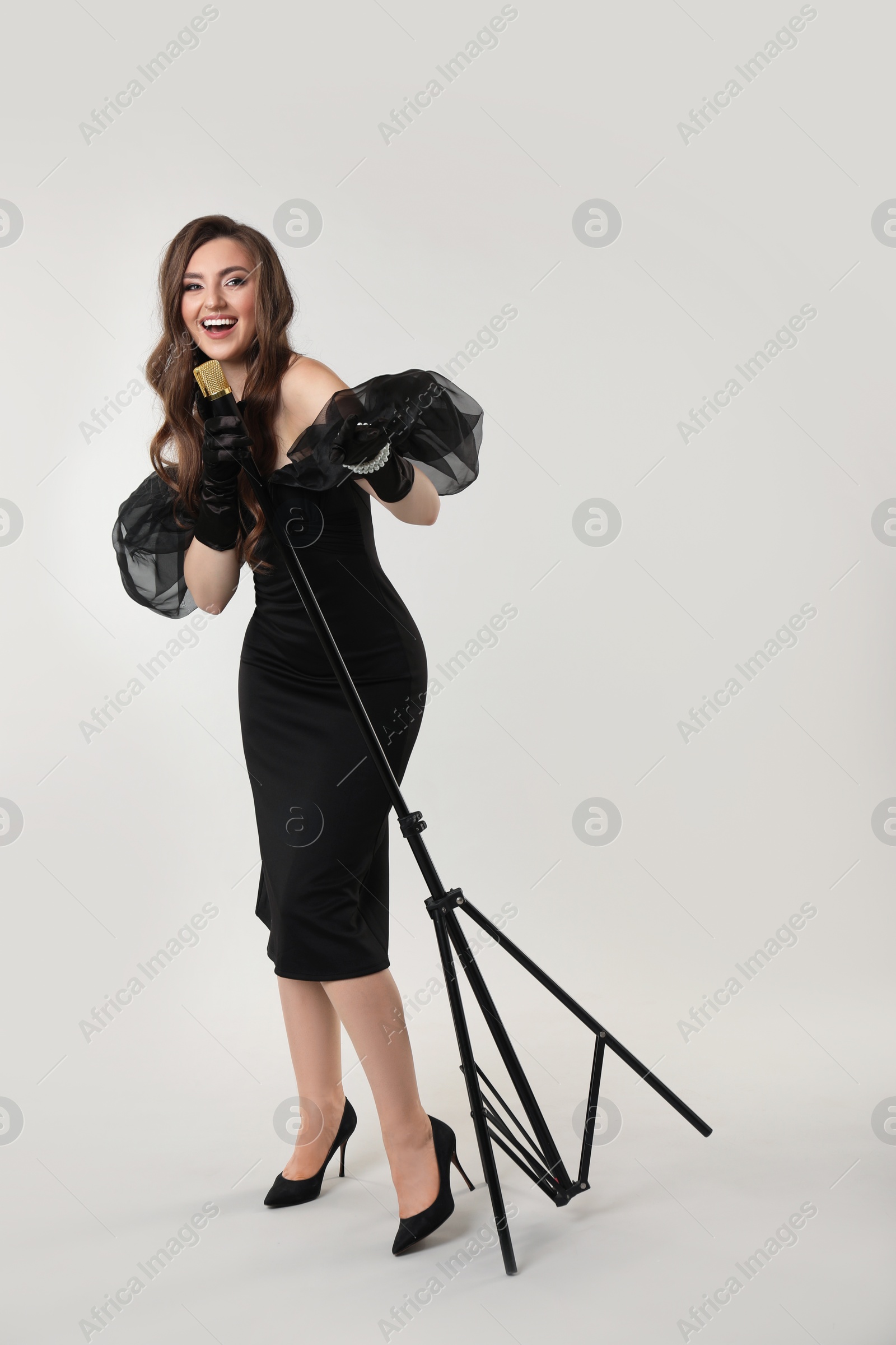 Photo of Beautiful young woman in stylish dress with microphone singing on light grey background