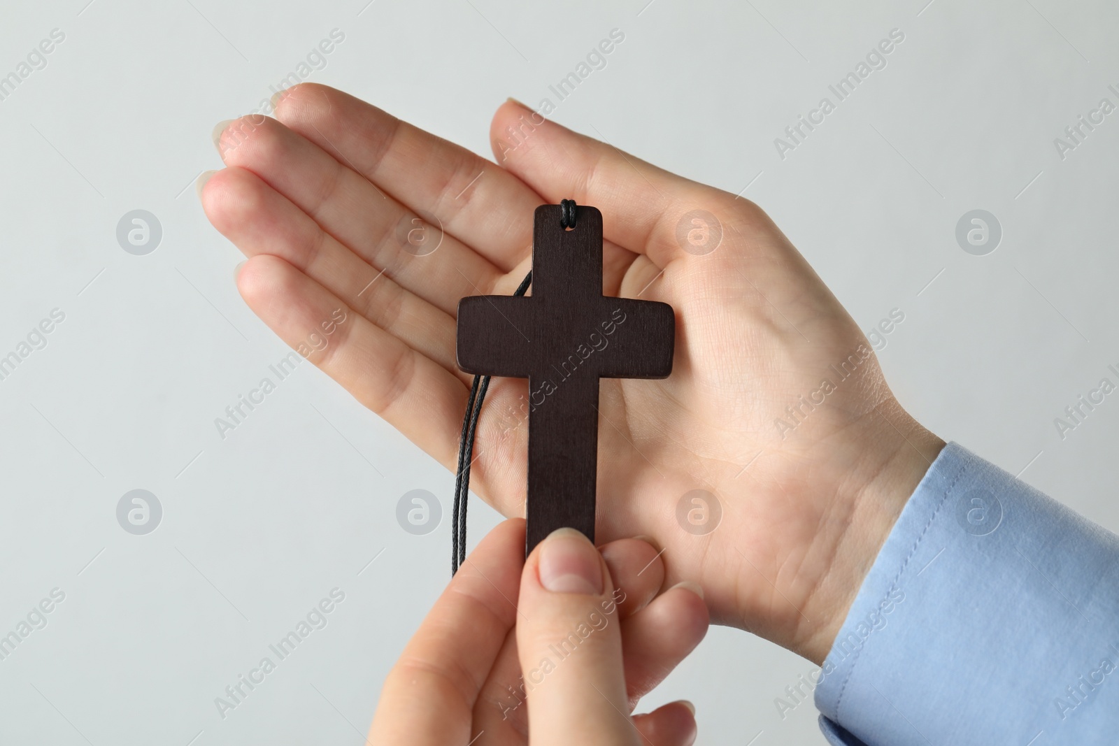 Photo of Woman holding wooden Christian cross on light grey background, closeup