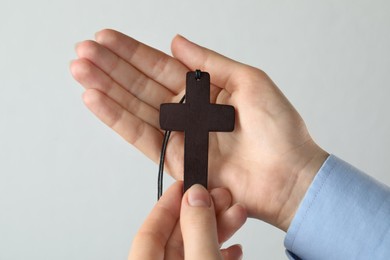 Woman holding wooden Christian cross on light grey background, closeup