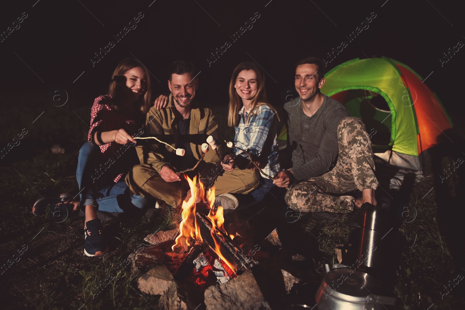 Photo of Friends frying marshmallows on bonfire at night. Camping season
