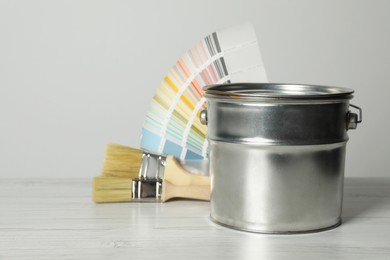 Can of paint, color palette samples and brushes on white wooden table