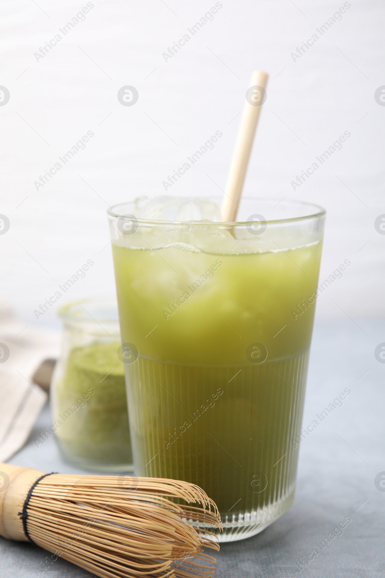 Photo of Glass of delicious iced green matcha tea and bamboo whisk on light grey table, closeup