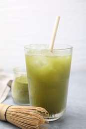 Photo of Glass of delicious iced green matcha tea and bamboo whisk on light grey table, closeup