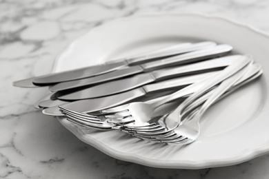 Photo of Plate with knives and forks on white marble table, closeup