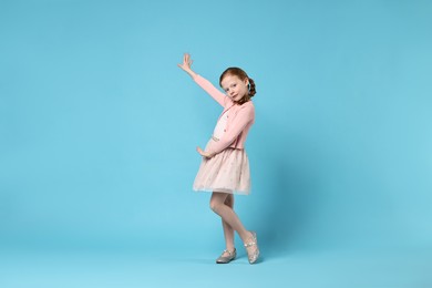 Photo of Cute little girl dancing on light blue background