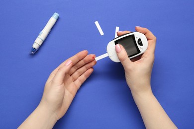 Photo of Diabetes. Woman checking blood sugar level with glucometer on blue background, top view