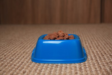 Photo of Wet pet food in feeding bowl on soft carpet indoors