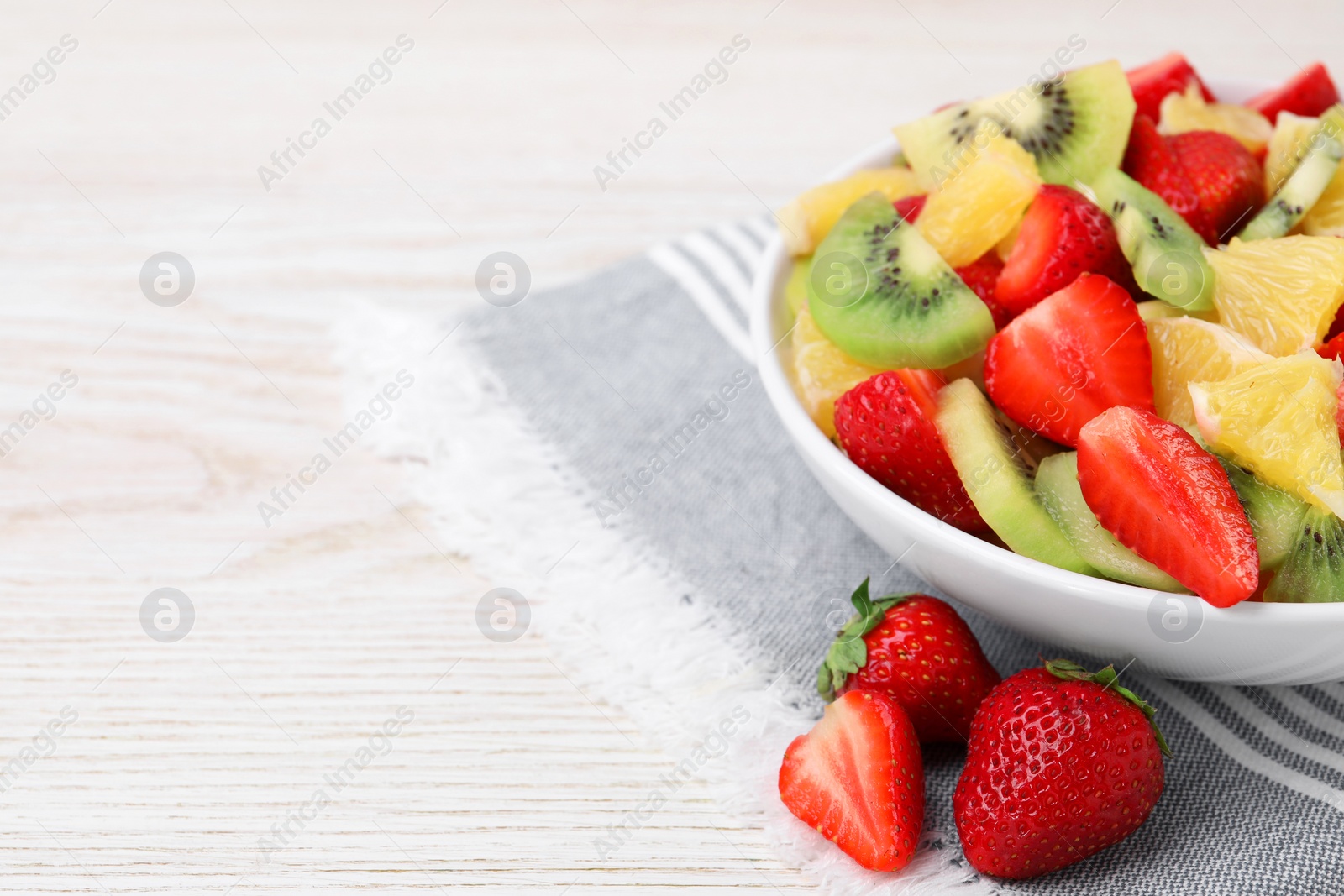 Photo of Delicious fresh fruit salad in bowl on white wooden table, closeup. Space for text