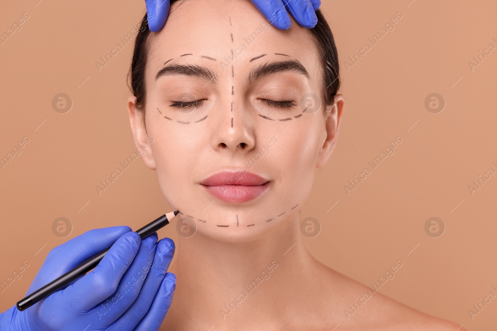 Photo of Doctor drawing marks on woman's face for cosmetic surgery operation against beige background