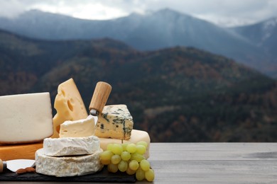 Photo of Different types of delicious cheeses and snacks on wooden table against mountain landscape. Space for text