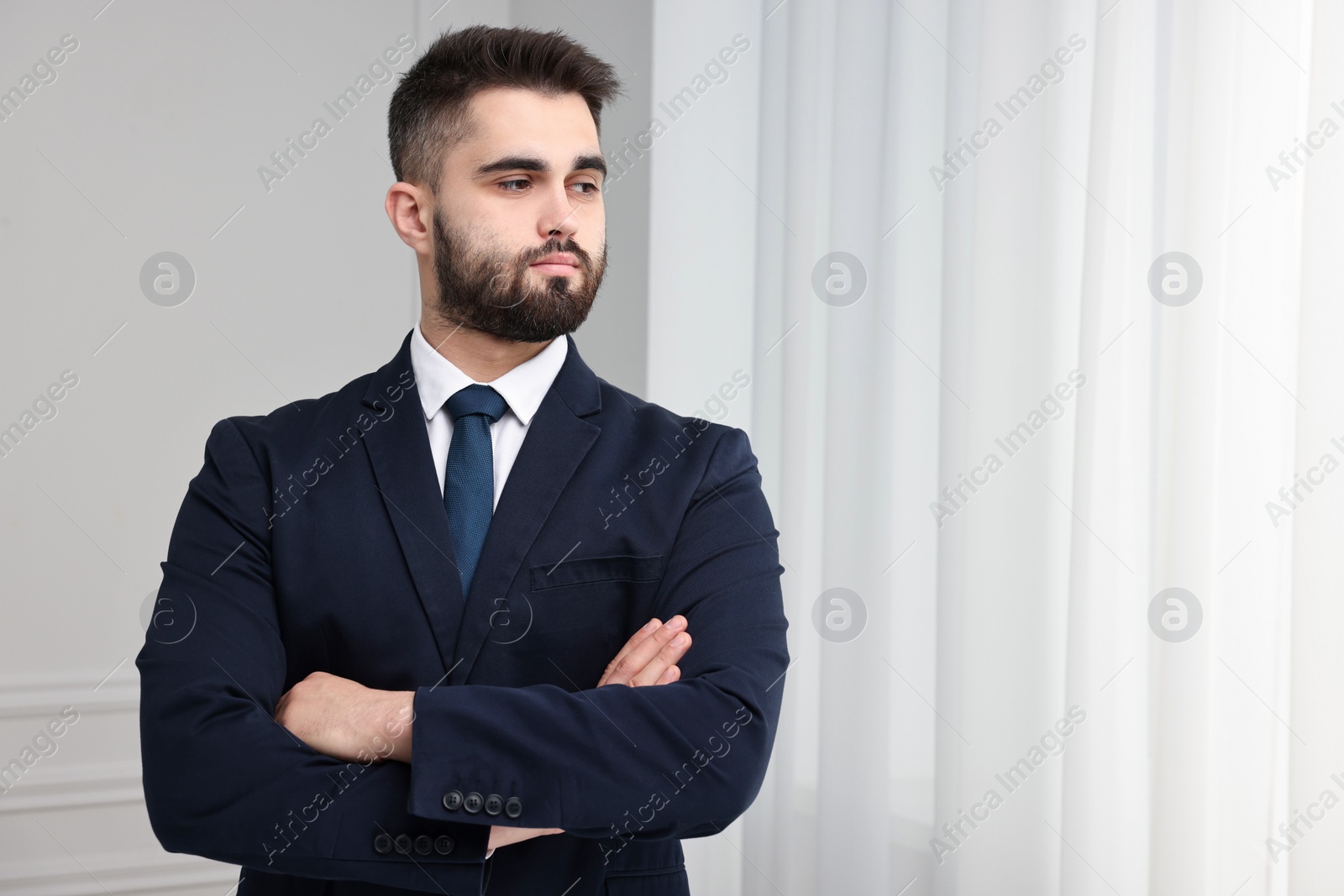 Photo of Handsome businessman in suit and necktie with crossed arms indoors. Space for text
