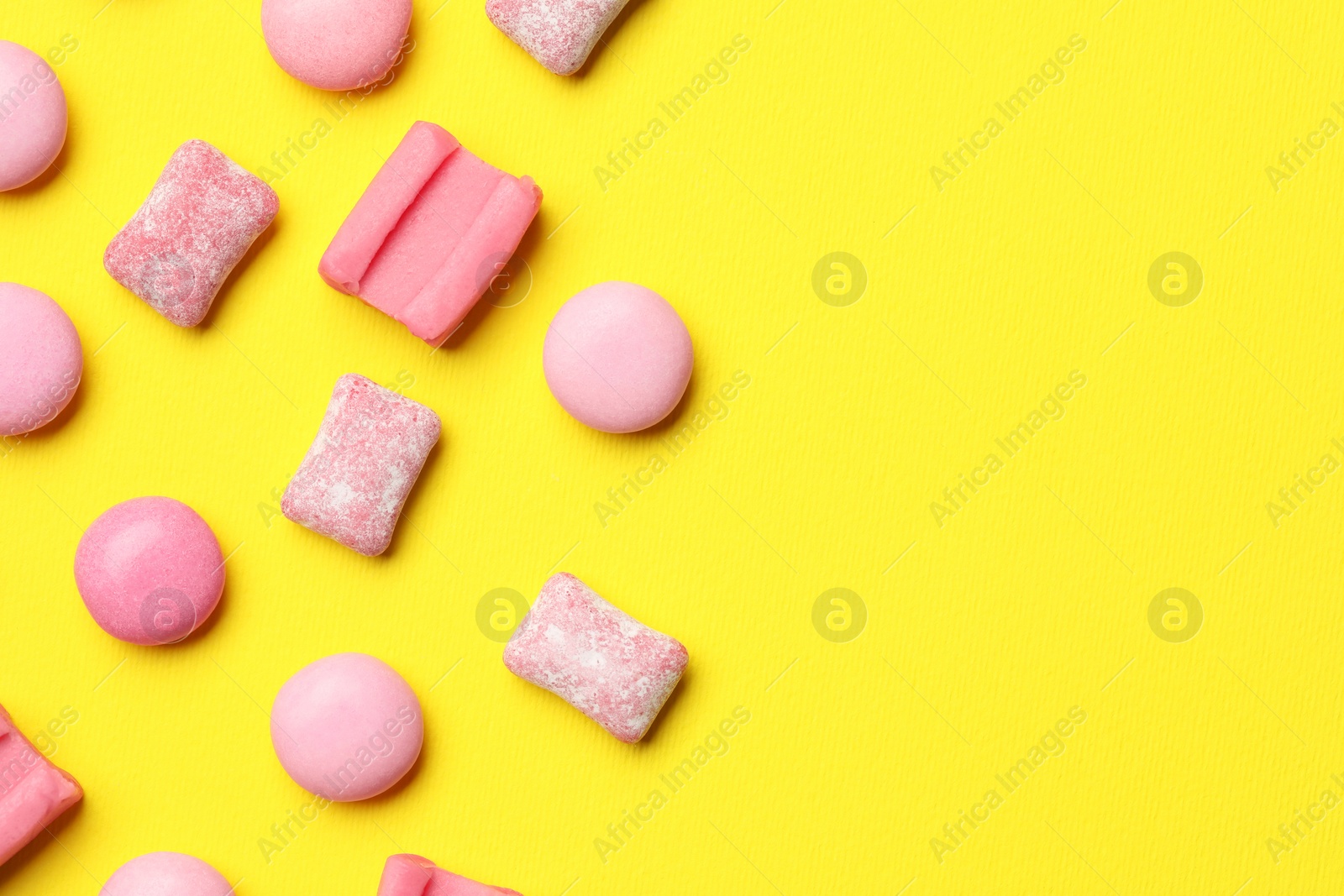 Photo of Pink bubble gums on yellow background, flat lay. Space for text