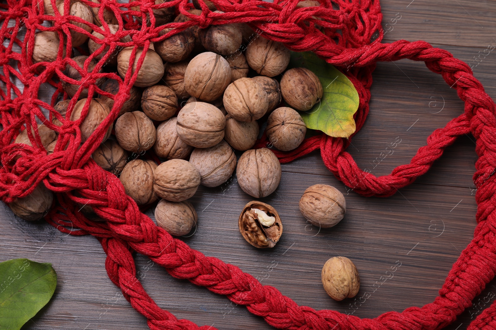 Photo of Net bag with walnuts and fresh leaves on wooden table, flat lay