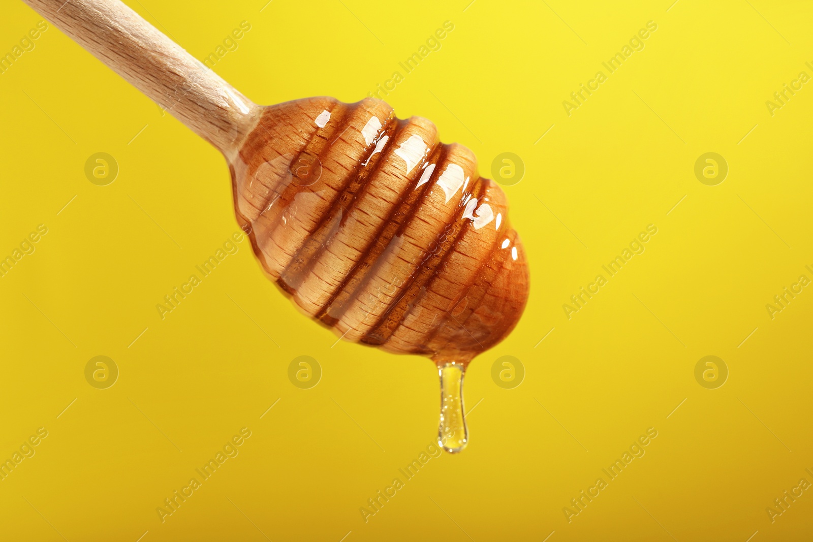 Photo of Delicious honey flowing down from dipper against yellow background, closeup