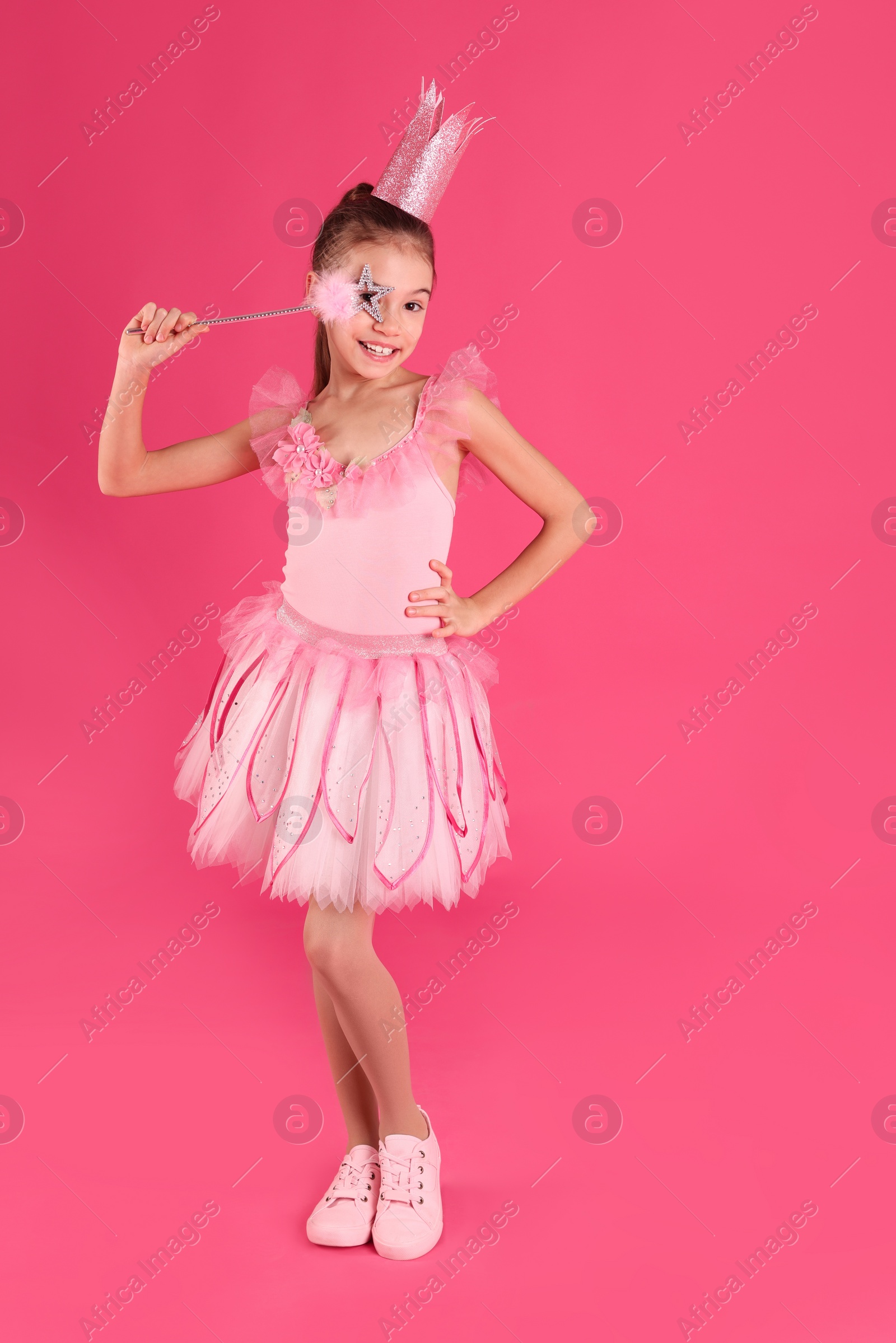 Photo of Cute girl in fairy dress with crown and magic wand on pink background. Little princess