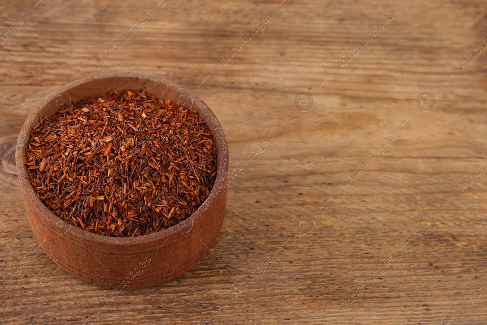 Photo of Dry rooibos leaves in bowl on wooden table, space for text