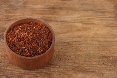 Dry rooibos leaves in bowl on wooden table, space for text