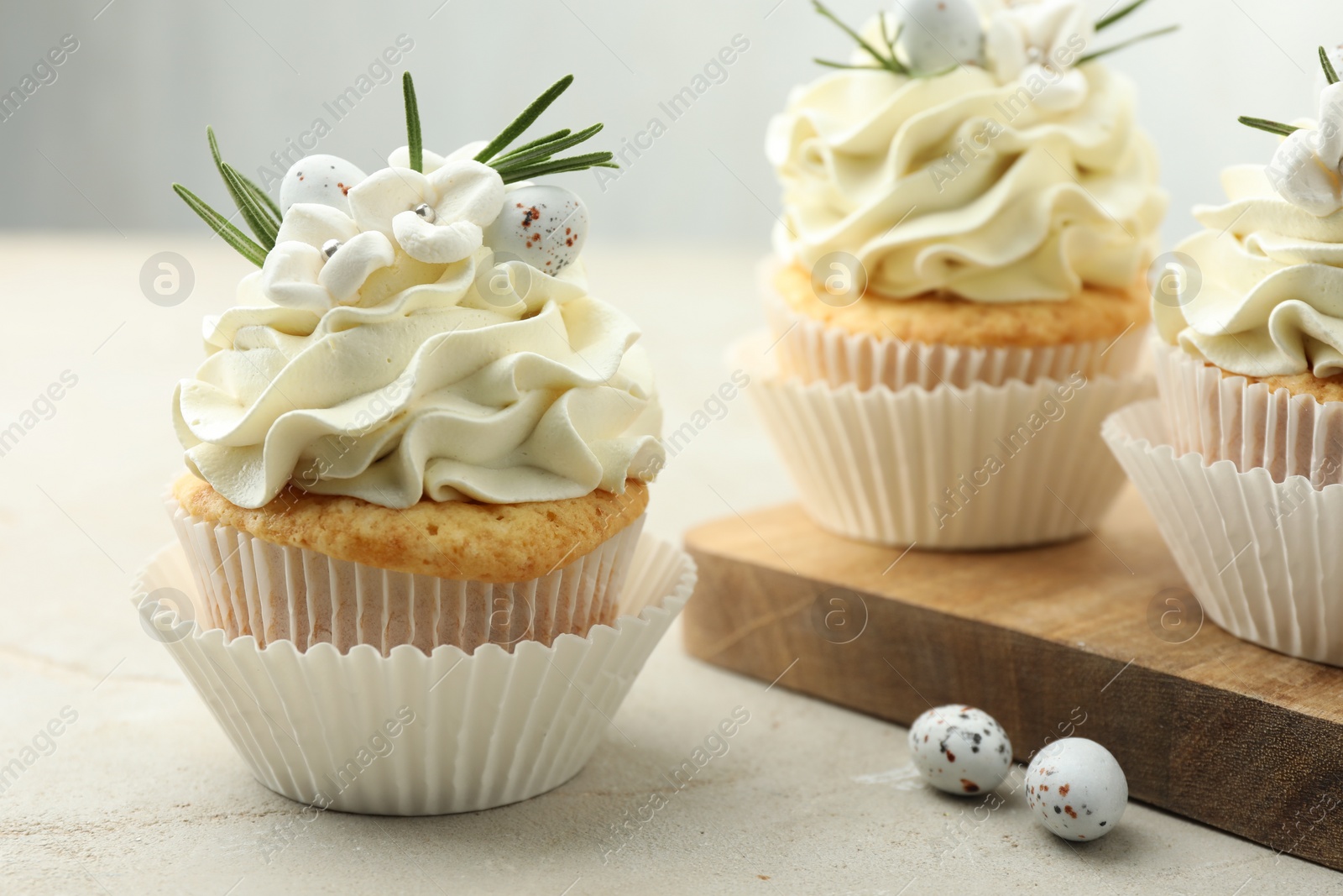 Photo of Tasty Easter cupcakes with vanilla cream and candies on gray table, closeup