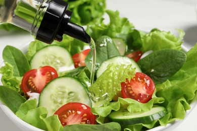 Photo of Pouring oil into delicious salad in bowl, closeup