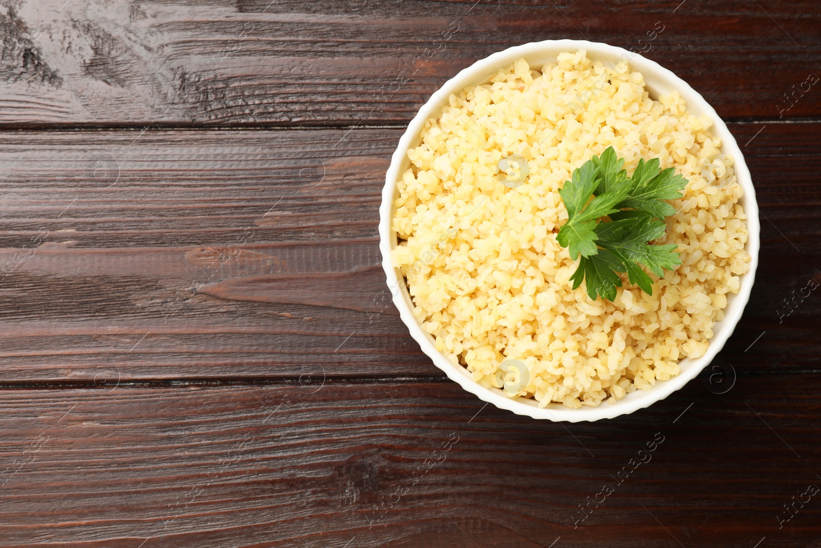 Photo of Delicious bulgur with parsley in bowl on wooden table, top view. Space for text