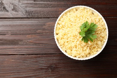 Delicious bulgur with parsley in bowl on wooden table, top view. Space for text