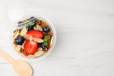 Photo of Tasty granola with berries, almond flakes and mint in plastic cup on white wooden table, top view. Space for text