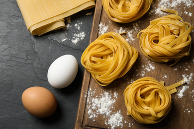 Raw tagliatelle pasta and products on black table, flat lay