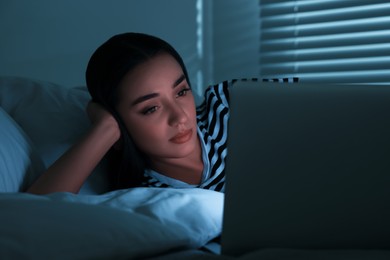 Young woman using laptop on bed at night. Internet addiction