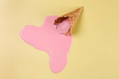 Photo of Melted ice cream and wafer cone on pale yellow background, top view