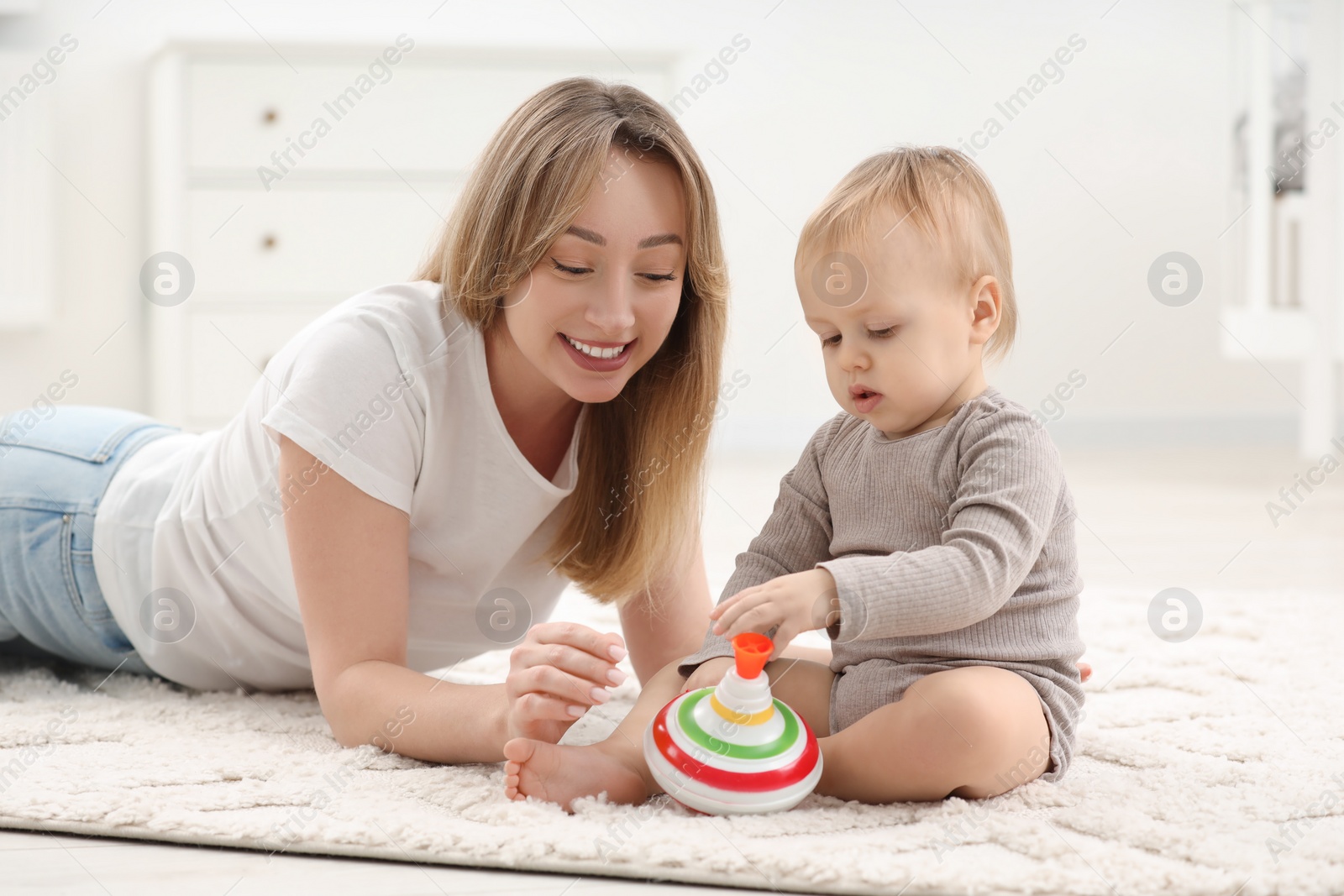 Photo of Children toys. Happy mother and her little son playing with spinning top on rug at home