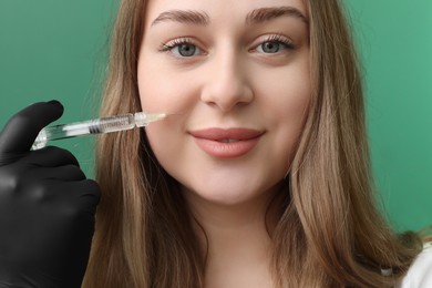 Photo of Cosmetologist with syringe on green background, closeup