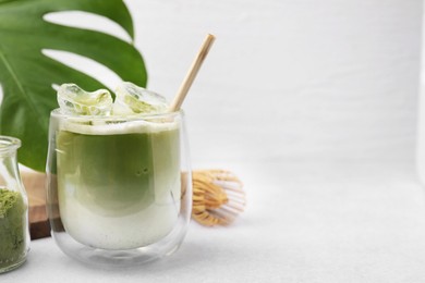 Photo of Glass of tasty iced matcha latte, leaf and bamboo whisk on white table. Space for text