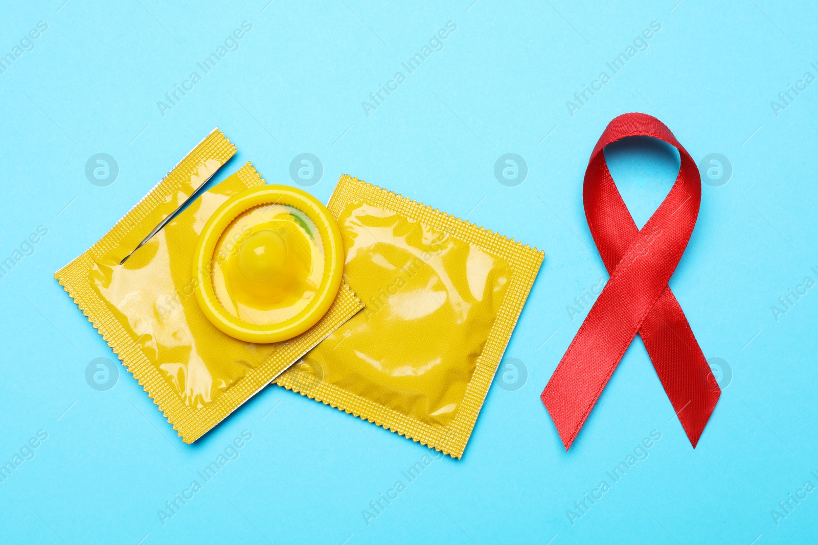 Photo of Yellow condoms and red ribbon on light blue background, flat lay. LGBT concept