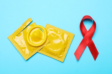 Photo of Yellow condoms and red ribbon on light blue background, flat lay. LGBT concept