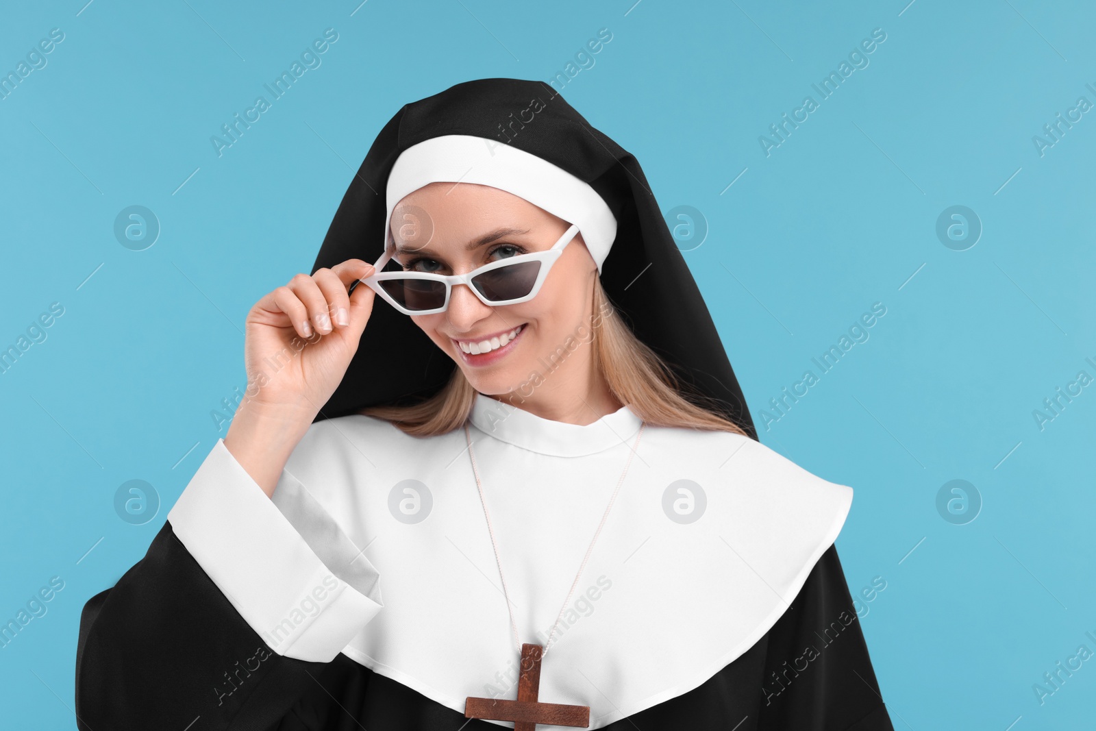 Photo of Happy woman in nun habit and sunglasses against light blue background