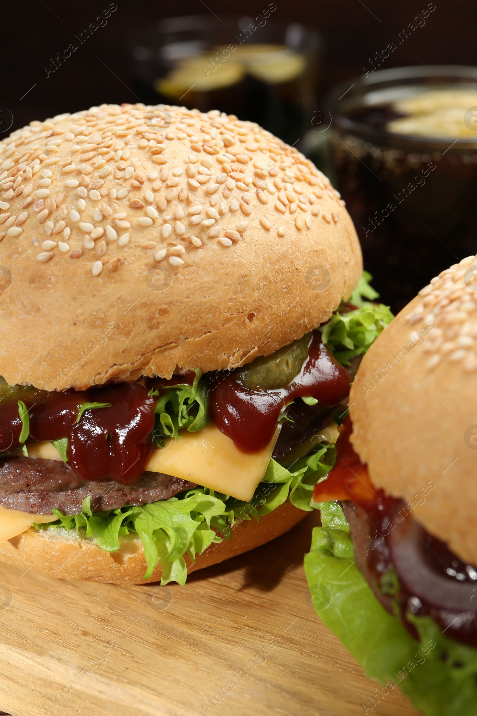 Photo of Wooden board with delicious cheeseburgers against blurred background, closeup
